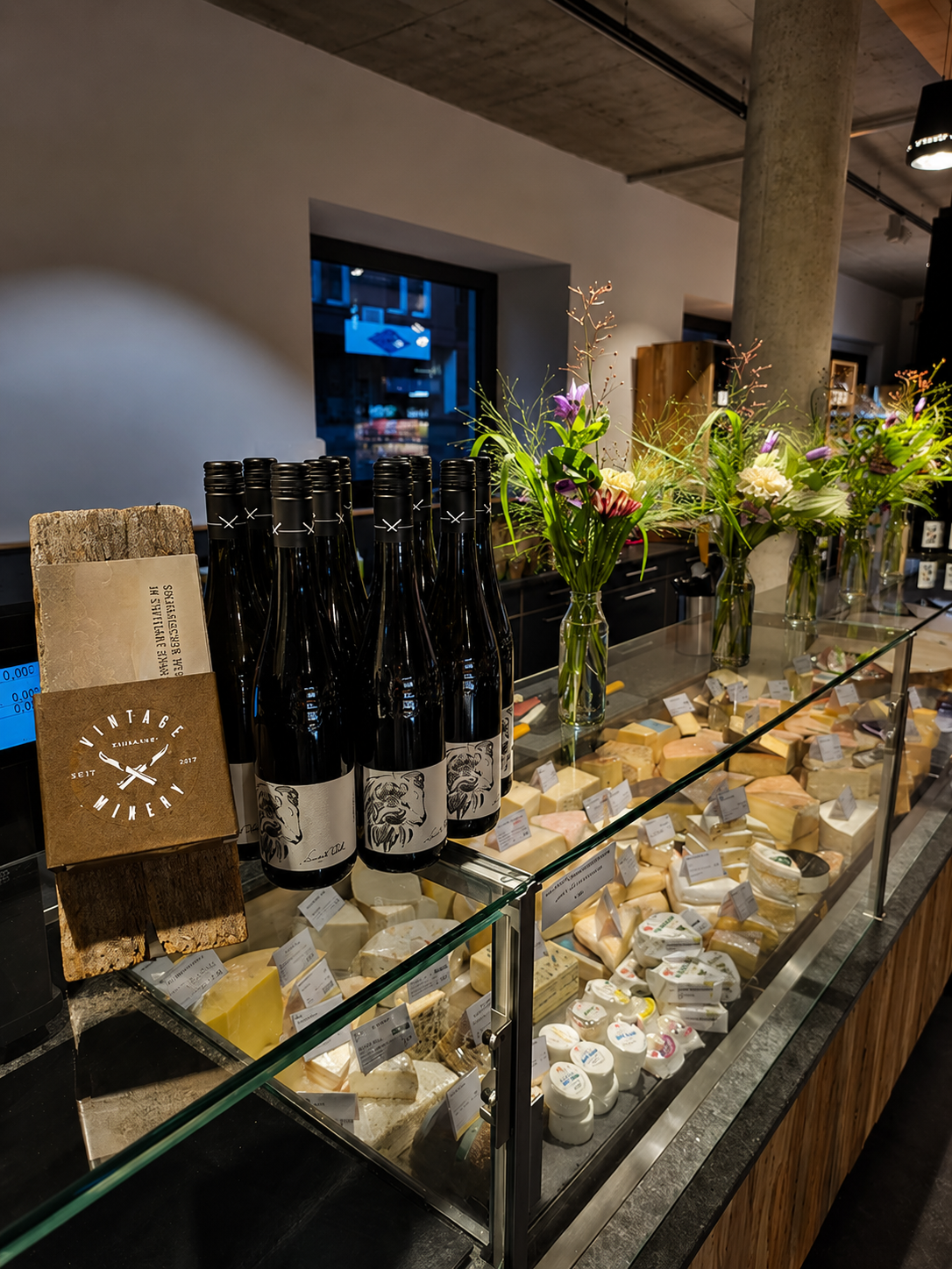 Käsetheke mit Weinen und frischen Blumen